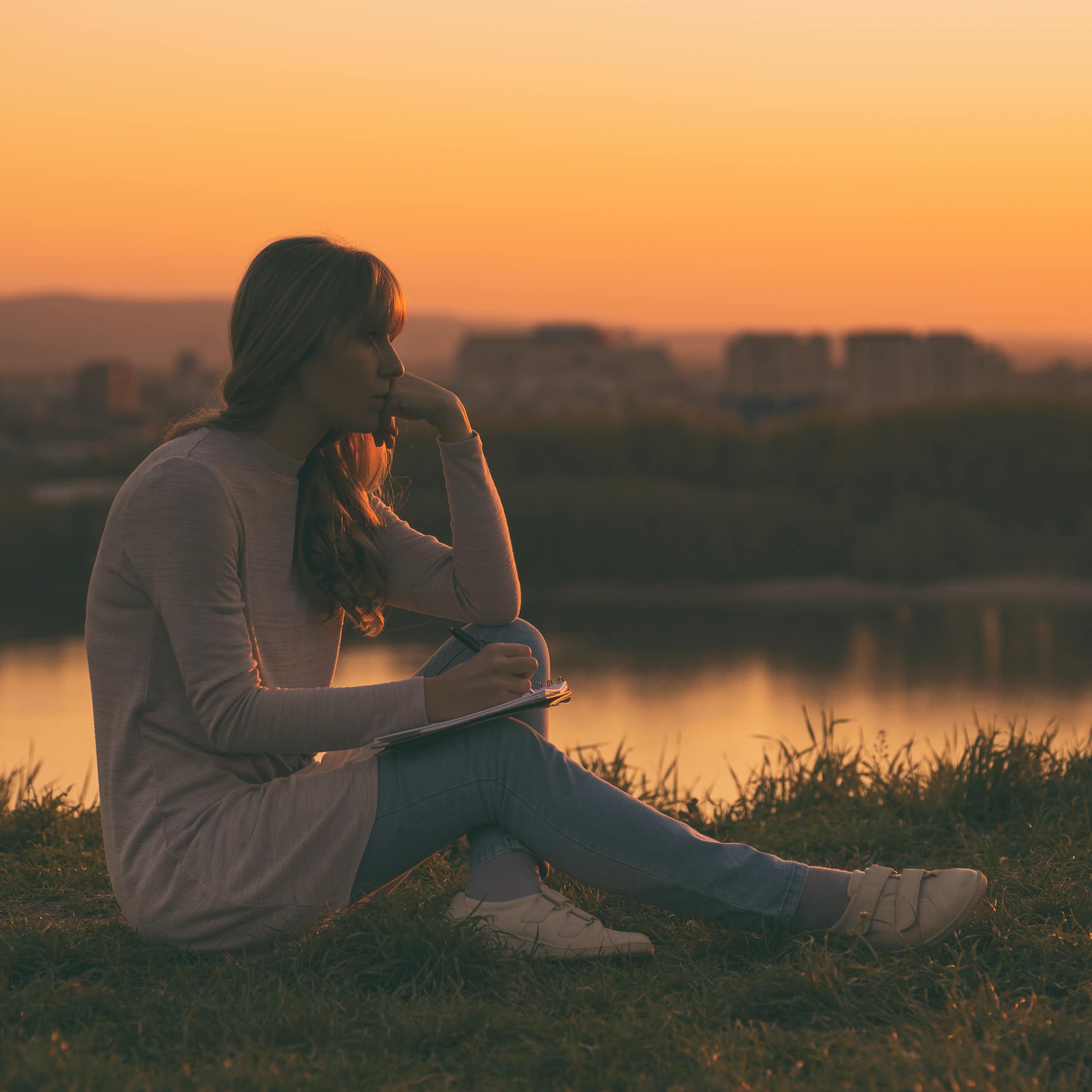 A woman looking pensive writing poetry at sunset