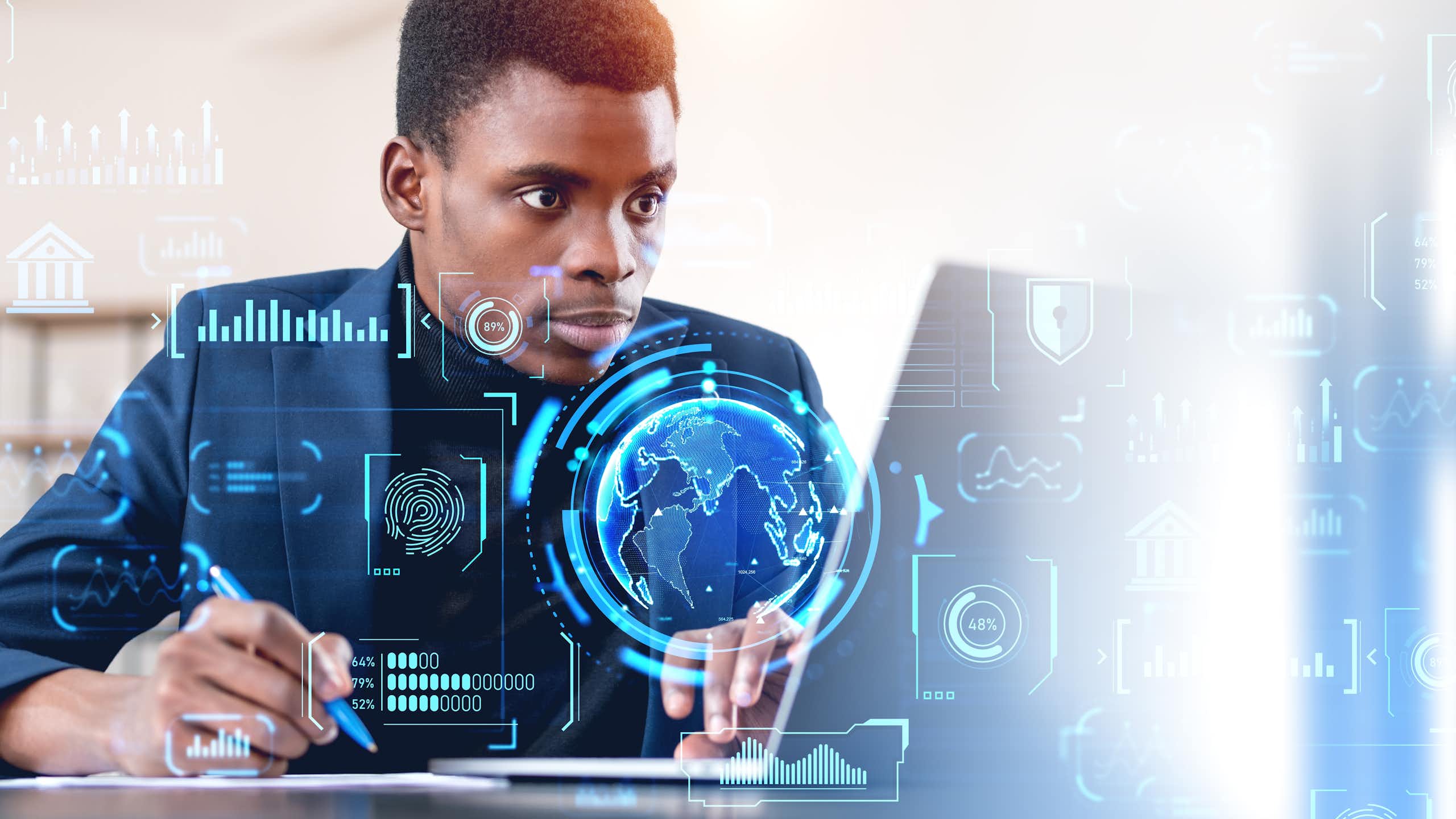 A man sits at a laptop while digital globes and graphs flash in the air around him, depicting his interaction with the digital economy