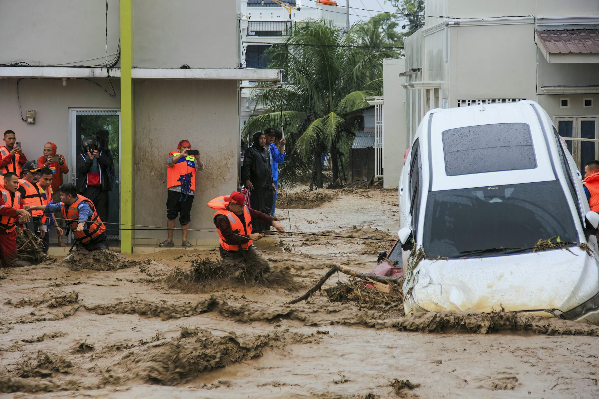 rescuers in floodwater with upended car.
