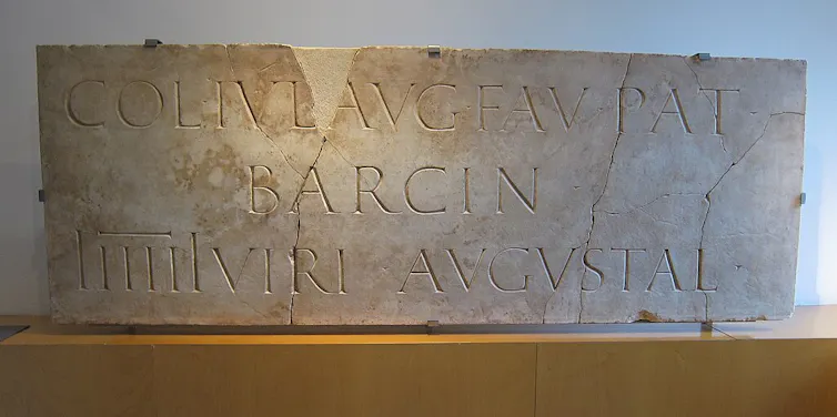 Un marbre romà amb text en llatí ('COL IVL AVG FAV PAT BARCIN', abreviatura de 'Colonia Julia Augusta Faventia Paterna Barcino') que descriu Barcino.