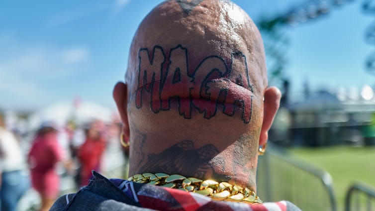 The back of a bald man's head with a tattoo reading: MAGA