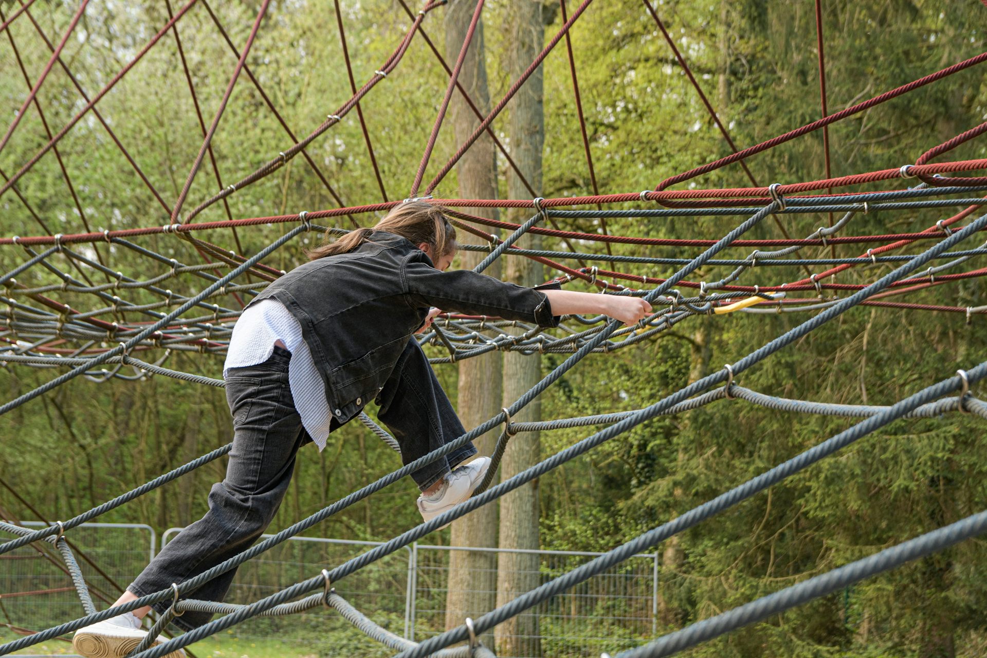 Teen girl on spiderweb ropes in playground