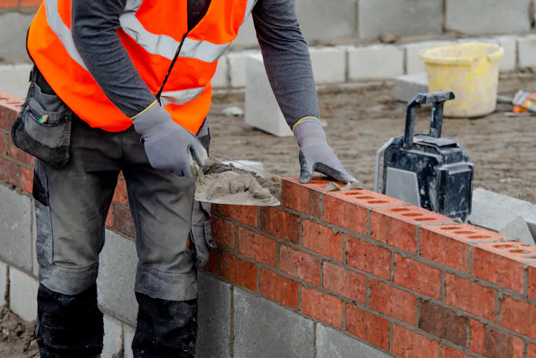 torso of a bricklayer adding mortar to a wall with a trowel
