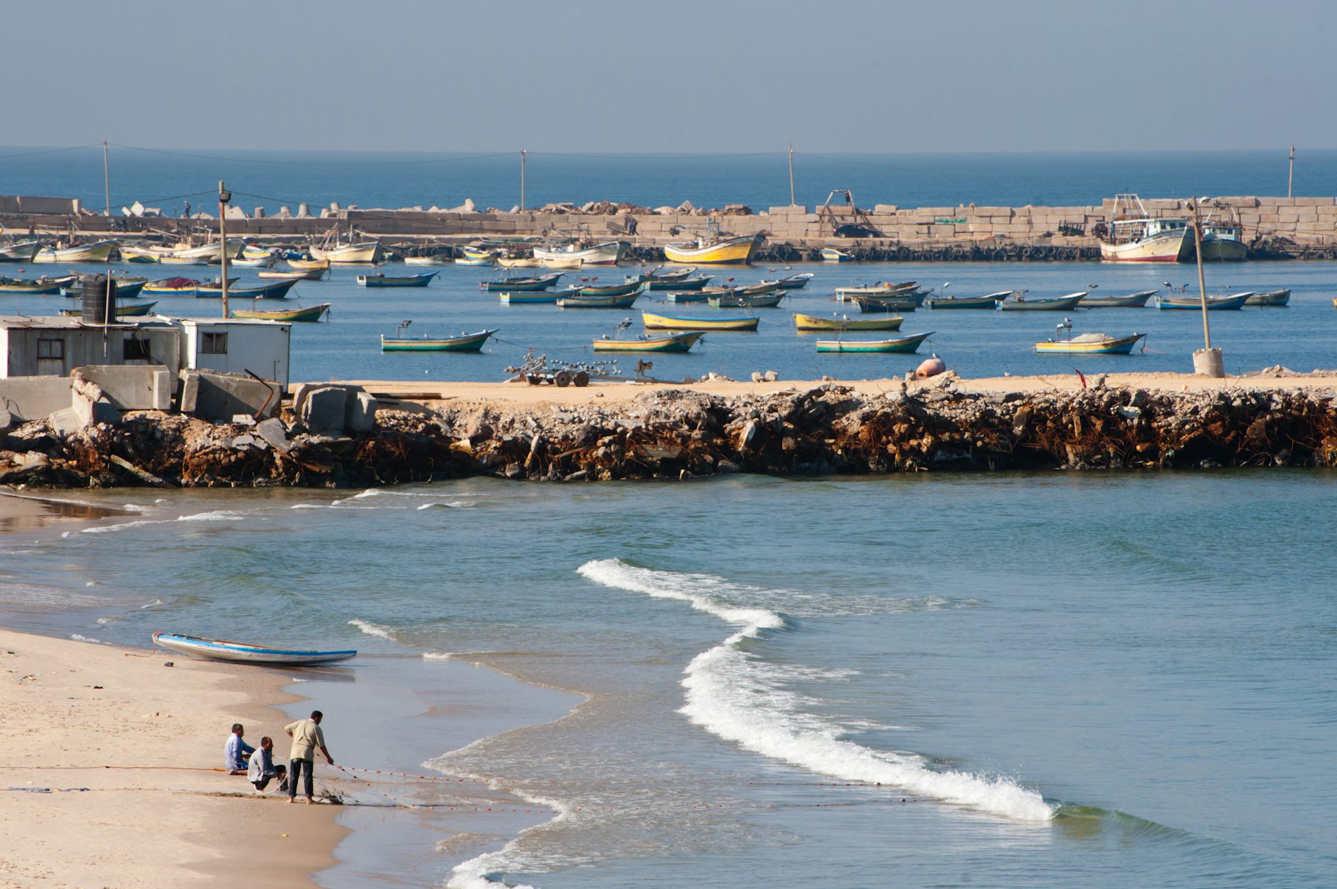 Gazan fishermen haul in their net on a beach next to a harbour/