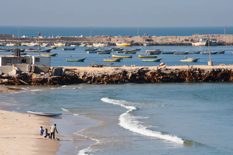 Gazan fishermen haul in their net on a beach next to a harbour/