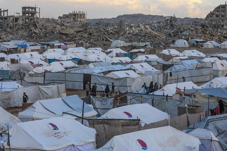 Tents of internally displaced Palestinians stand beside the ruins of destroyed buildings during a rainy day in Gaza City.
