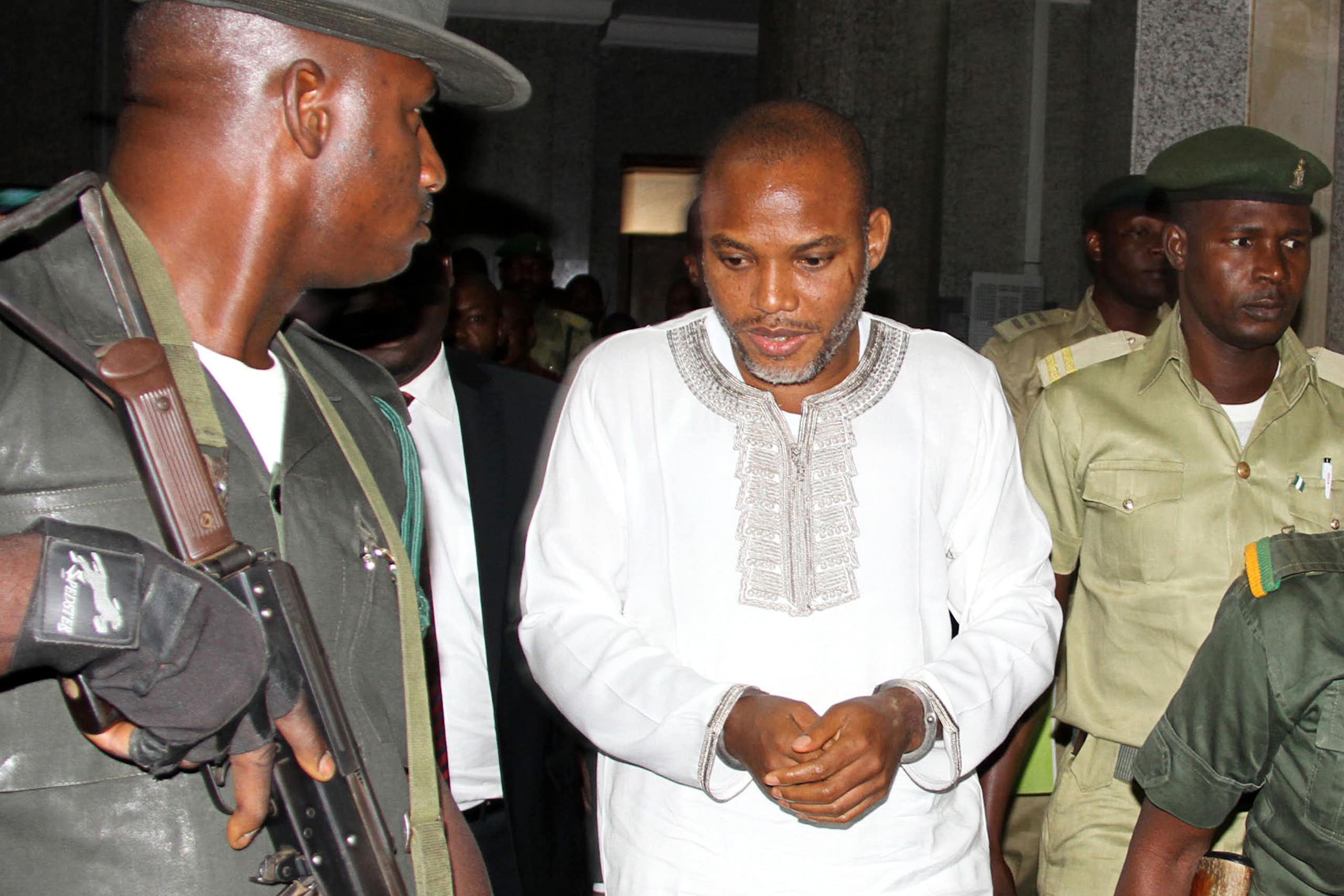 A man in white traditional dress surrounded by security officers