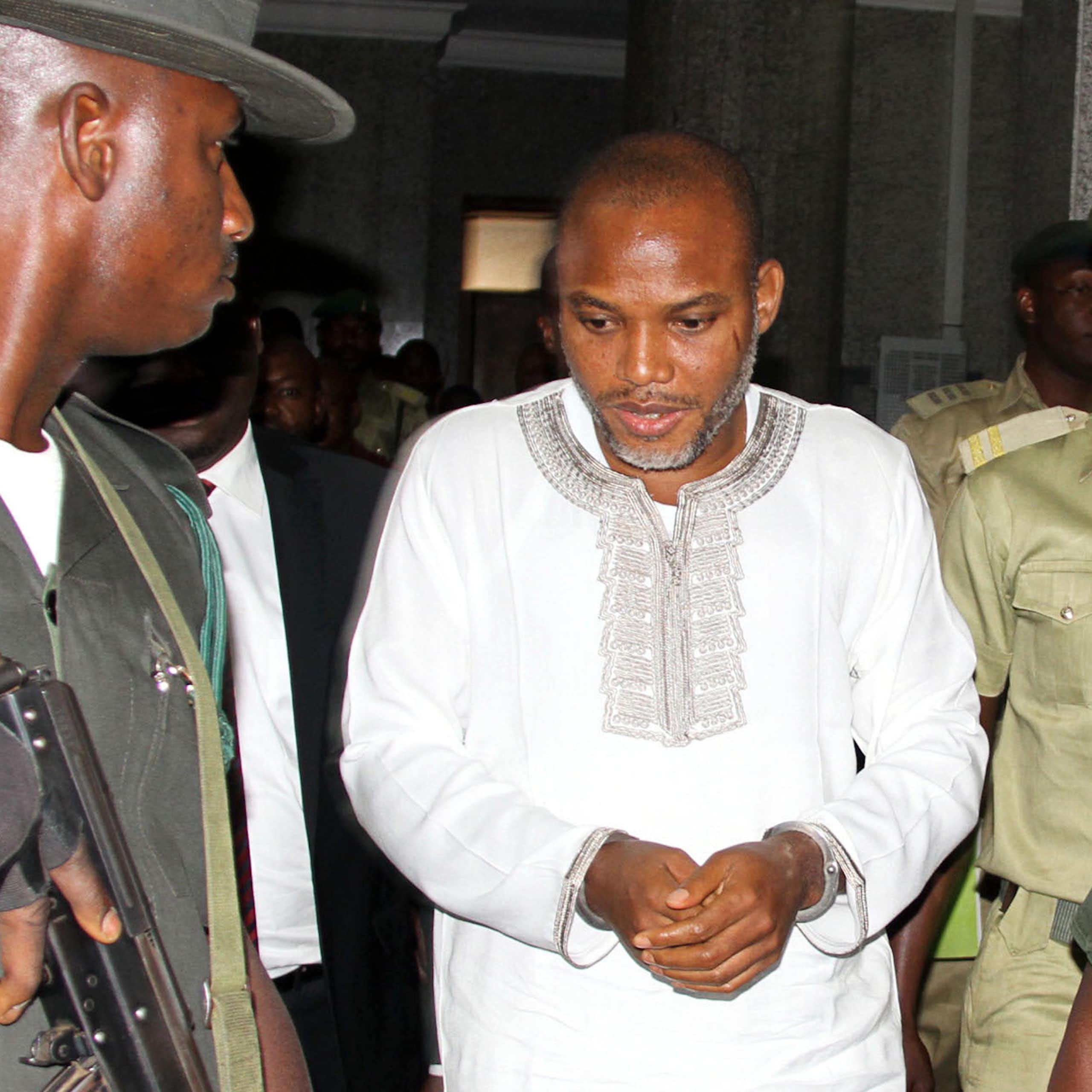 A man in white traditional dress surrounded by security officers