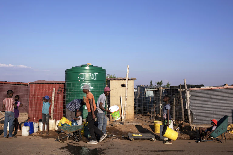 People lining up with buckets and carrying buckets of water in wheelbarrows - lining up at a 5000 litre water tank