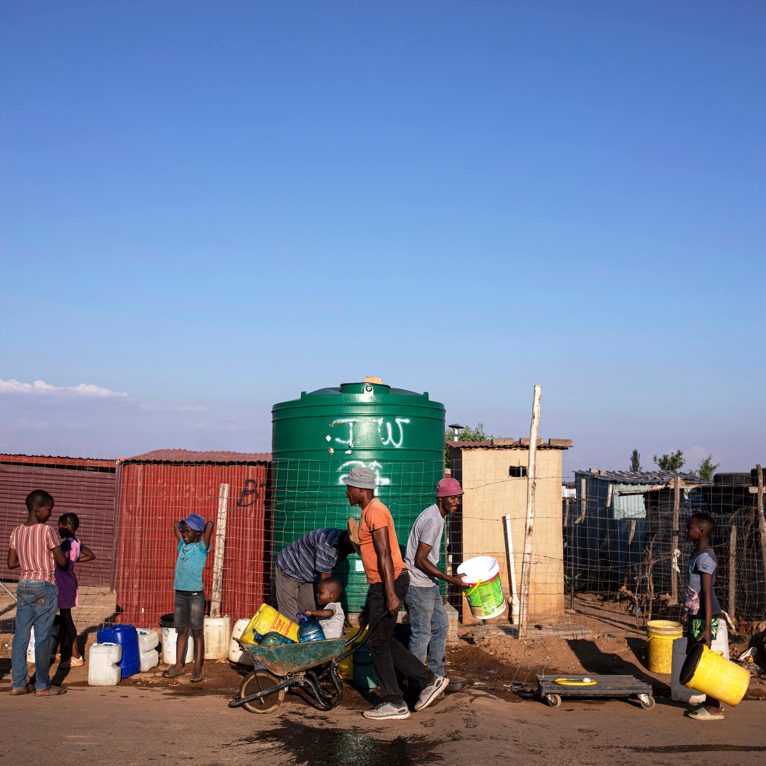 People lining up with buckets and carrying buckets of water in wheelbarrows - lining up at a 5000 litre water tank