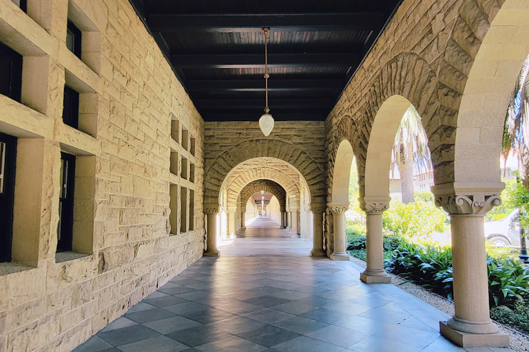 An empty hallway is seen surrounded by stone pillars and a stone wall.