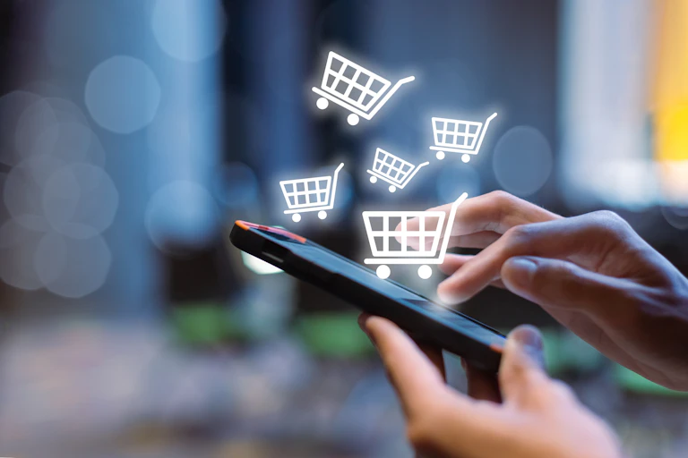 A woman's hands using a smartphone, graphic of supermarket trolley indicates online shopping