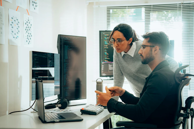 Two people look at a computer sitting on a desk