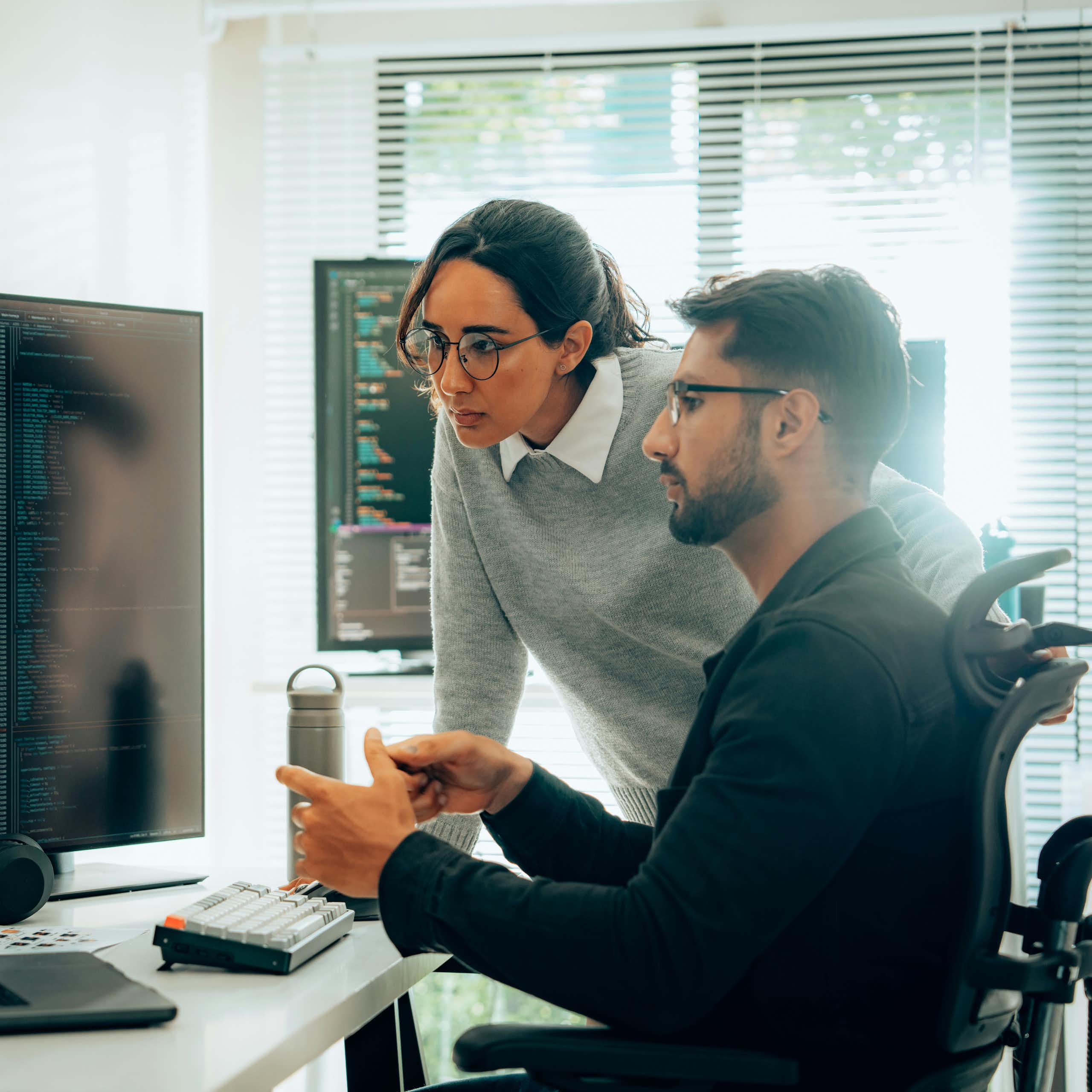Two people look at a computer sitting on a desk