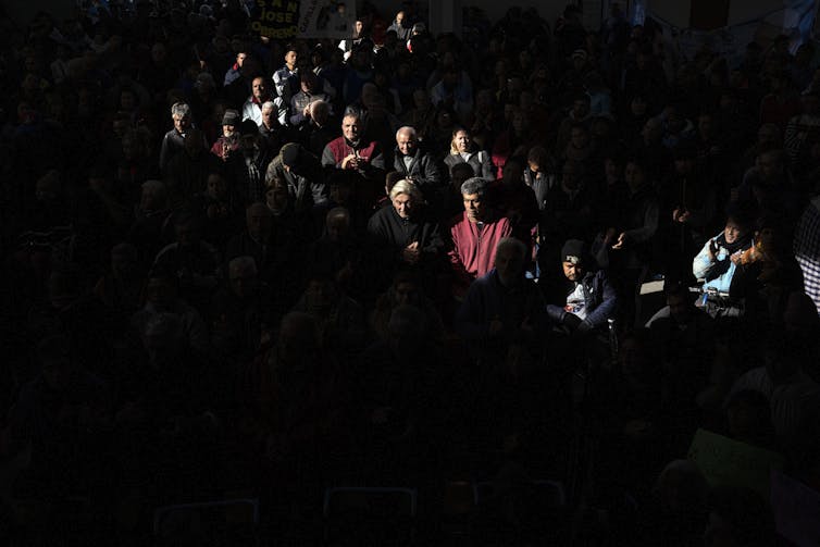 ‘Yes’ to God, however ‘no’ to church – what spiritual alternate seems like for lots of Latin American citizens 1 A spotlight shines on a zigzag row of people wearing jackets, with the rest of the crowd hidden in the dark.