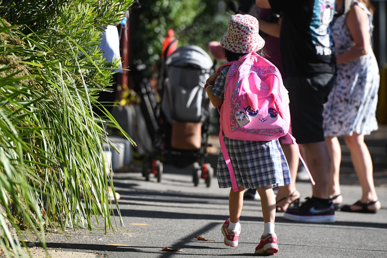 A young child walking in a back pack and uniform