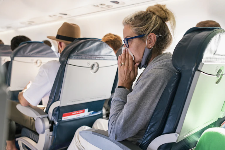 Older woman on plane blows her nose with a tissue.