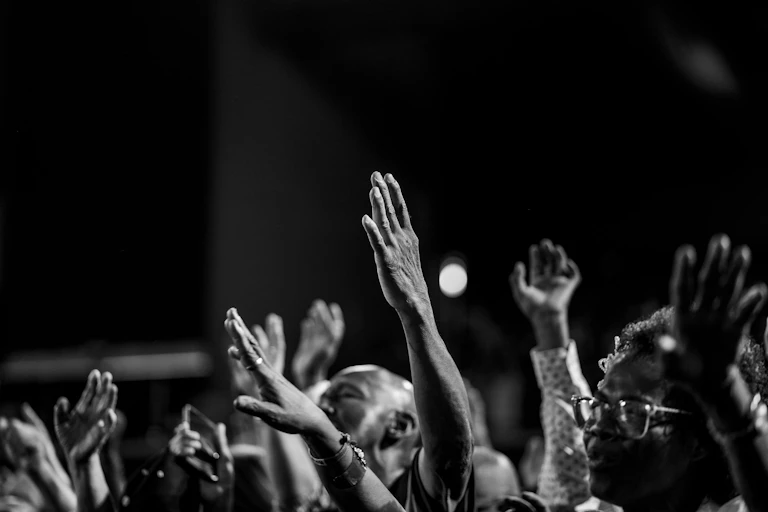 A black and white photo of Africans worshipping, hands in the air.