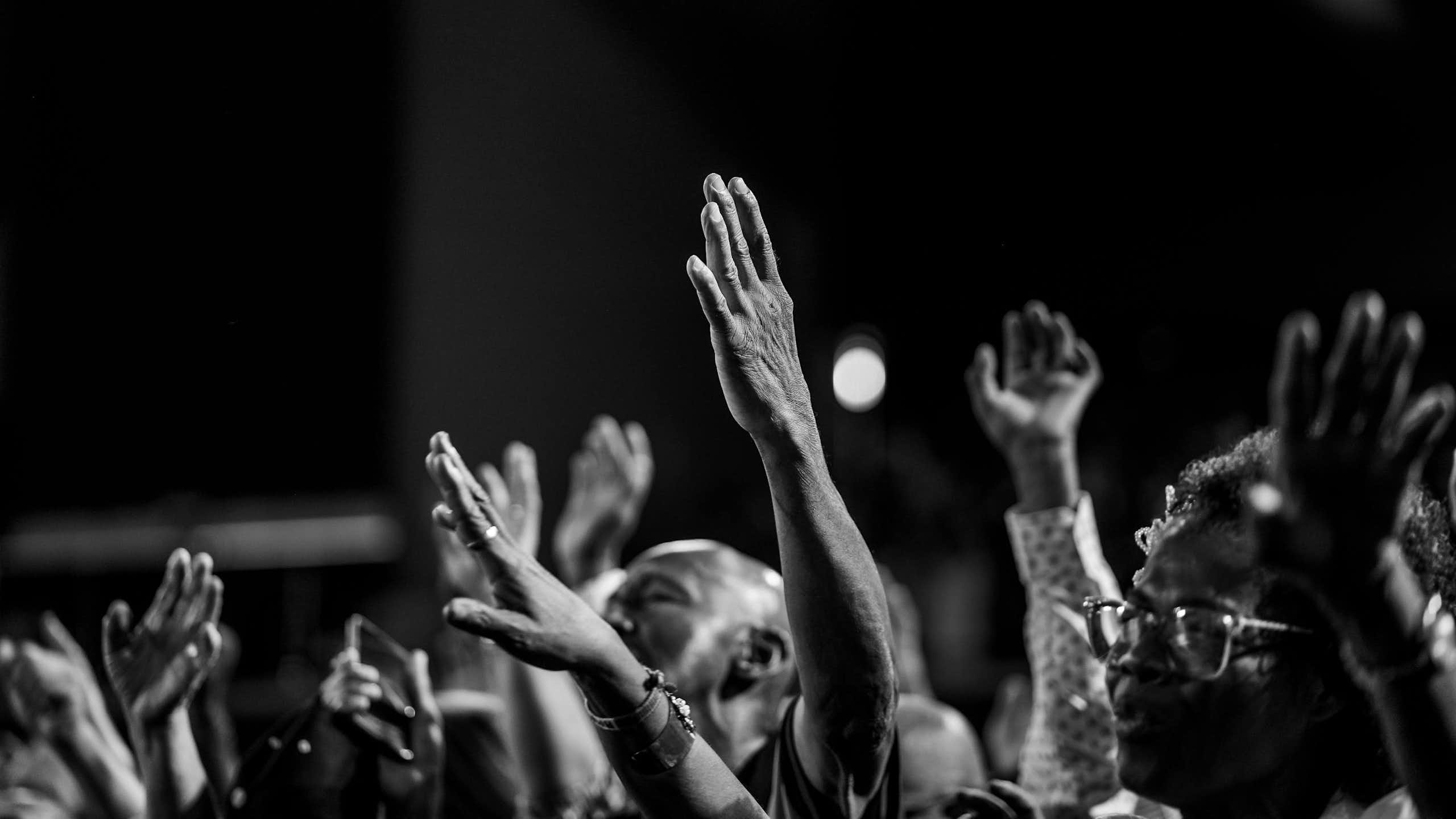 A black and white photo of Africans worshipping, hands in the air.