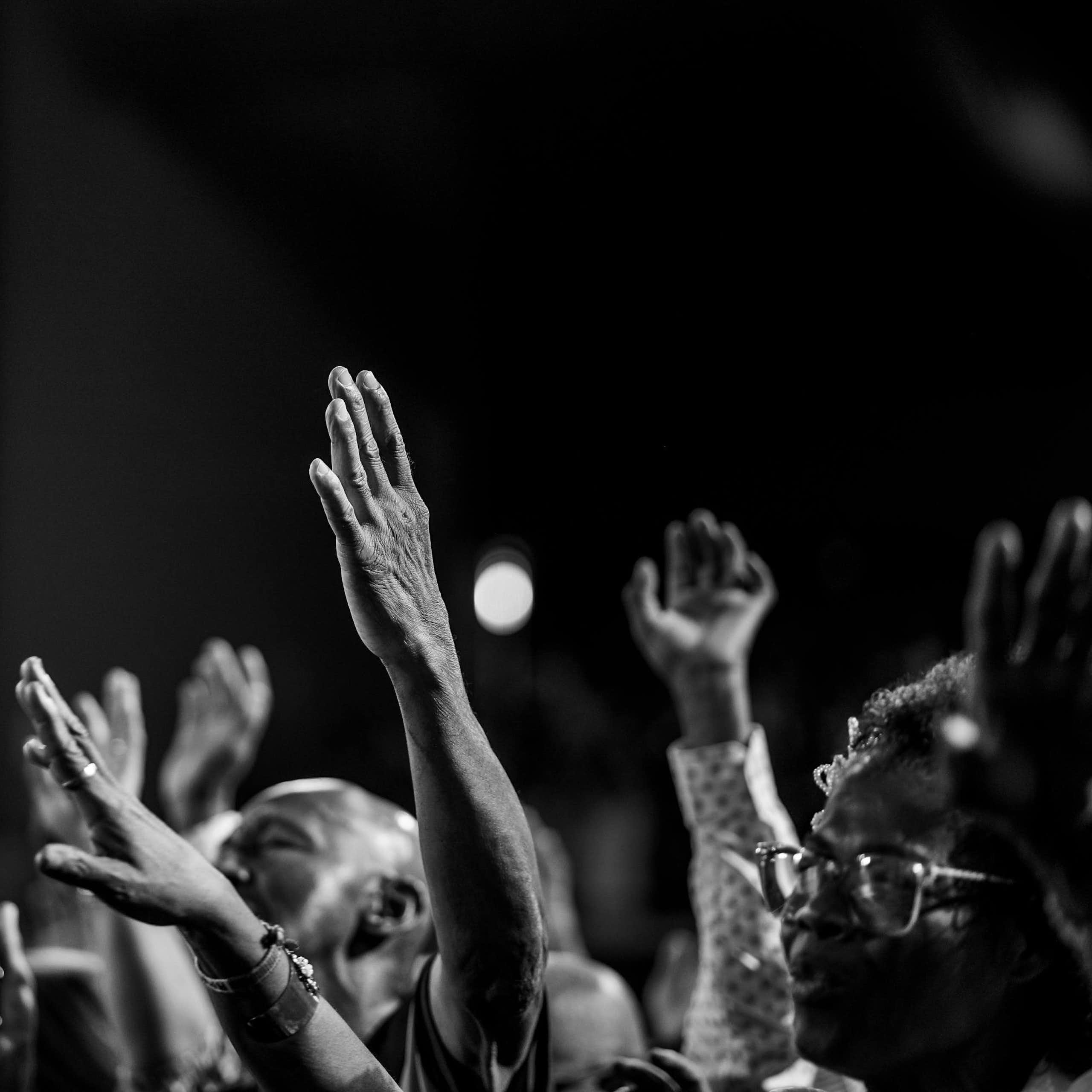 A black and white photo of Africans worshipping, hands in the air.