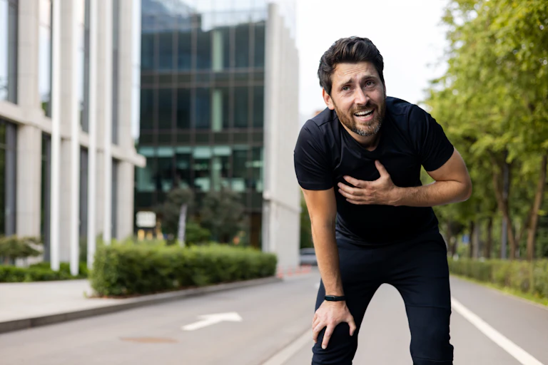 A man bends over, holding his hand on his chest.