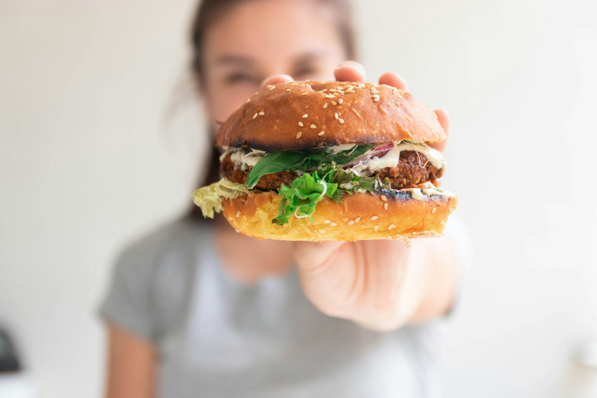 young woman holding up a plant-based burger in a bun