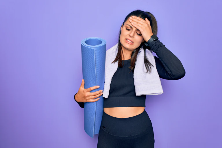 Woman holding yoga mat and cringing.