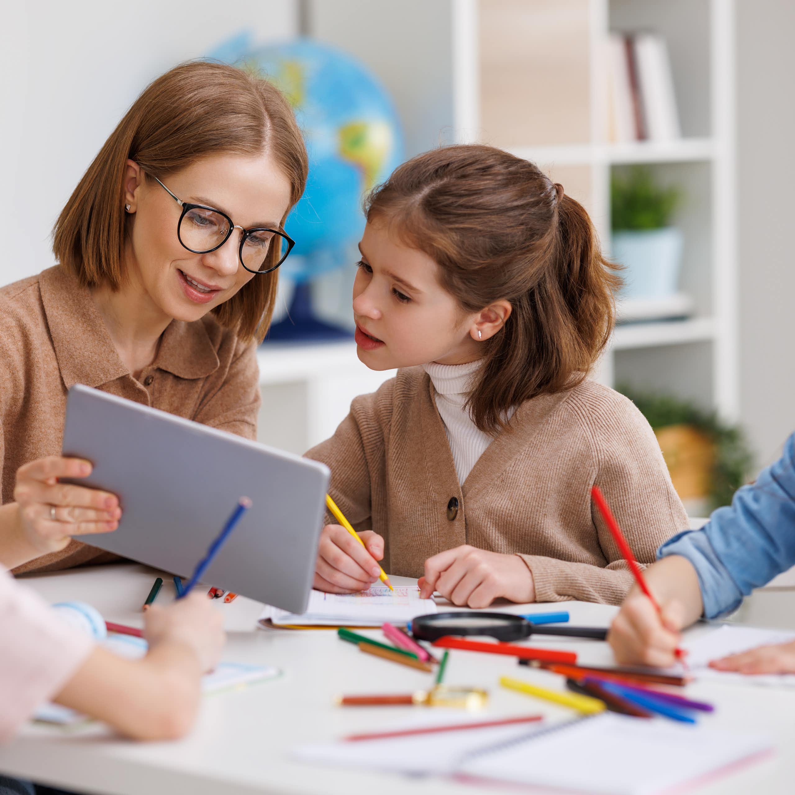 Una profesora enseña una tableta a una alumna.