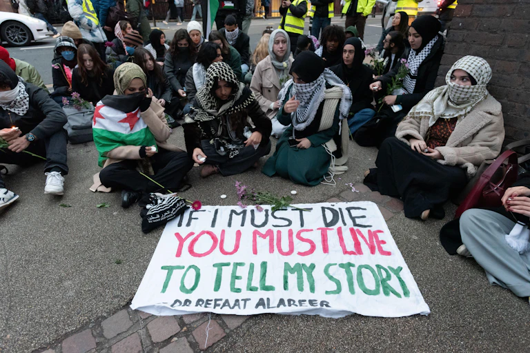 Students sitting round a sign that says "If I must die, you must live to tell my story"