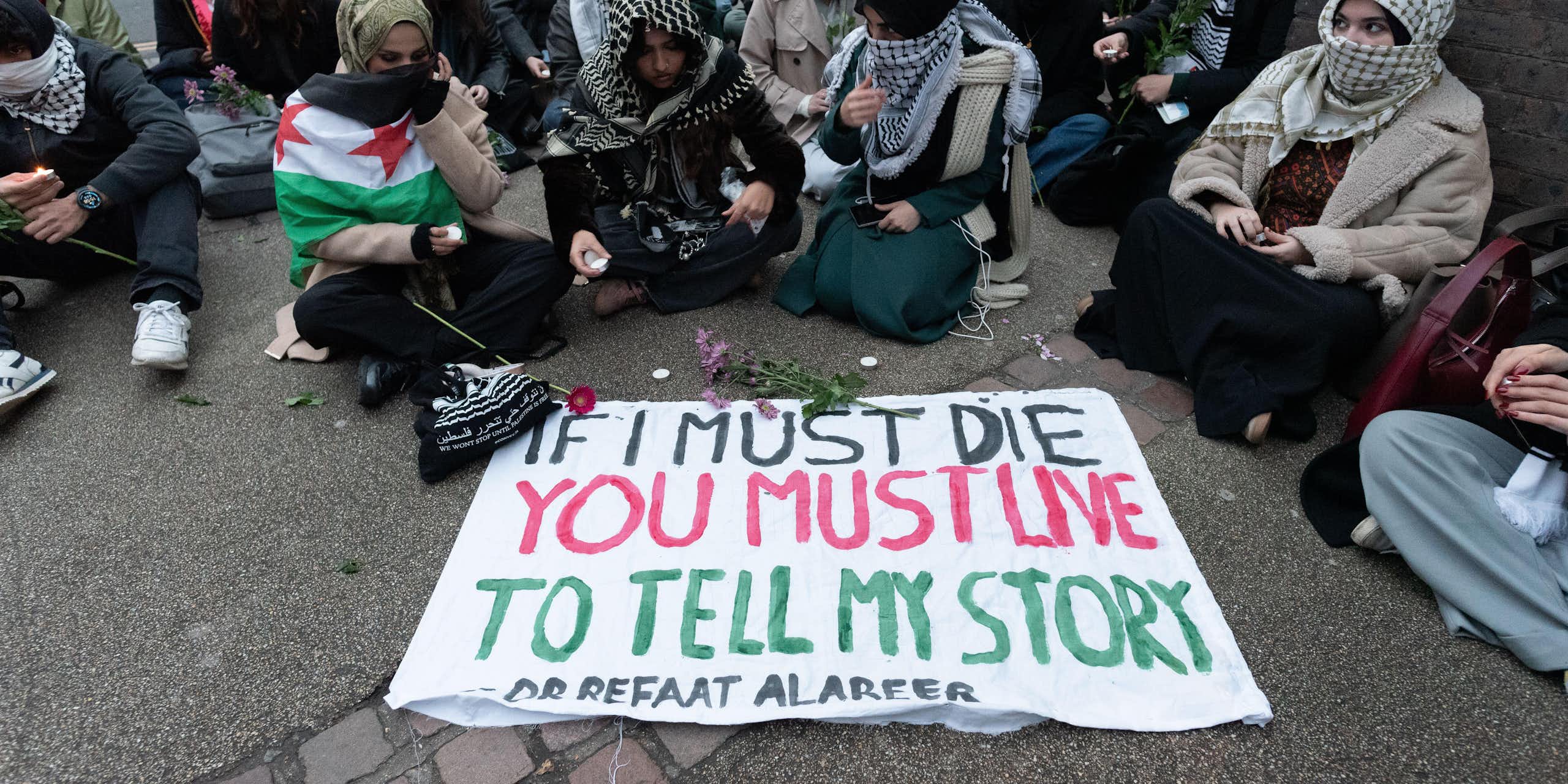Students sitting round a sign that says "If I must die, you must live to tell my story"