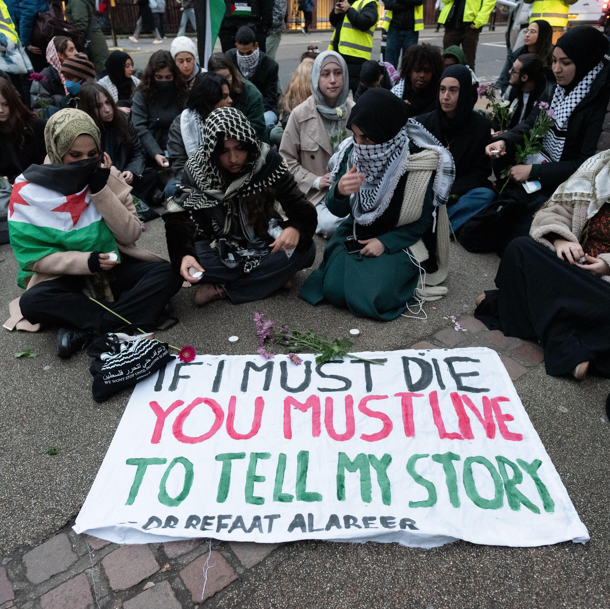 Students sitting round a sign that says "If I must die, you must live to tell my story"