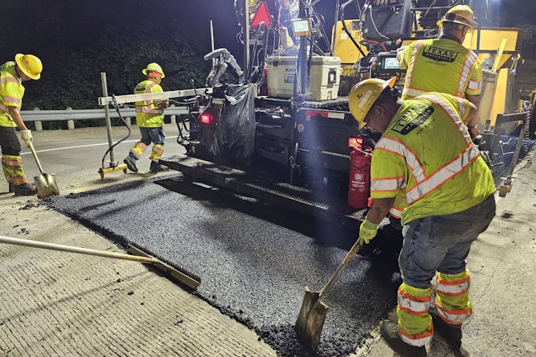 A team using shovels and broom-like tools to smooth a patch of new pavement.