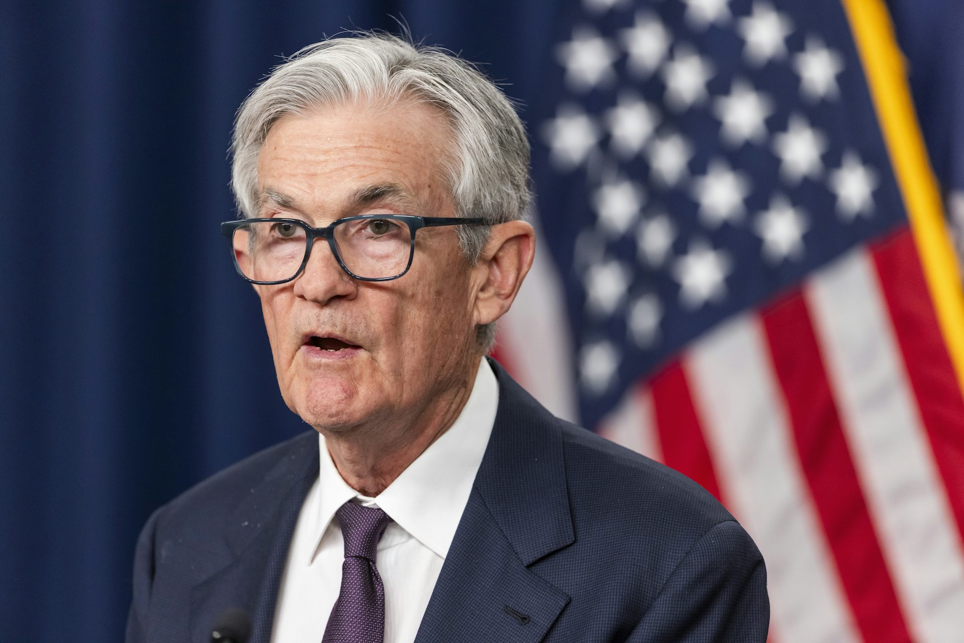 Jerome Powell announcing Fed interest-rate policy in front of a US flag.