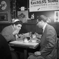 Merry Jewish Christmas: How Chinese language meals and the films turned into a time-honored custom for American Jews 1 A black and white photograph of two men in suit jackets and Jewish head coverings seated at a table with signs on the wall.