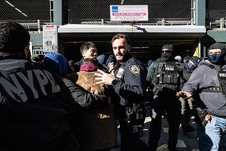 Are sanctuary policing insurance policies not more than a public family members facade? 1 Uniformed police officers push back a crowd of people.