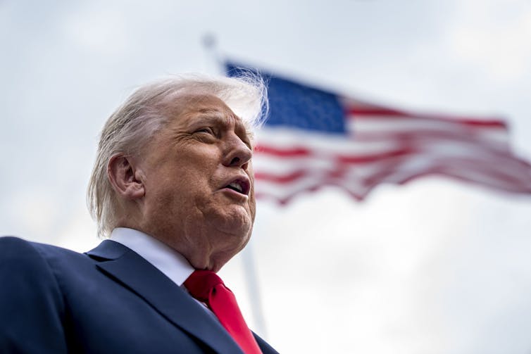 Donald Trump speaks to the press in front of a US flag.
