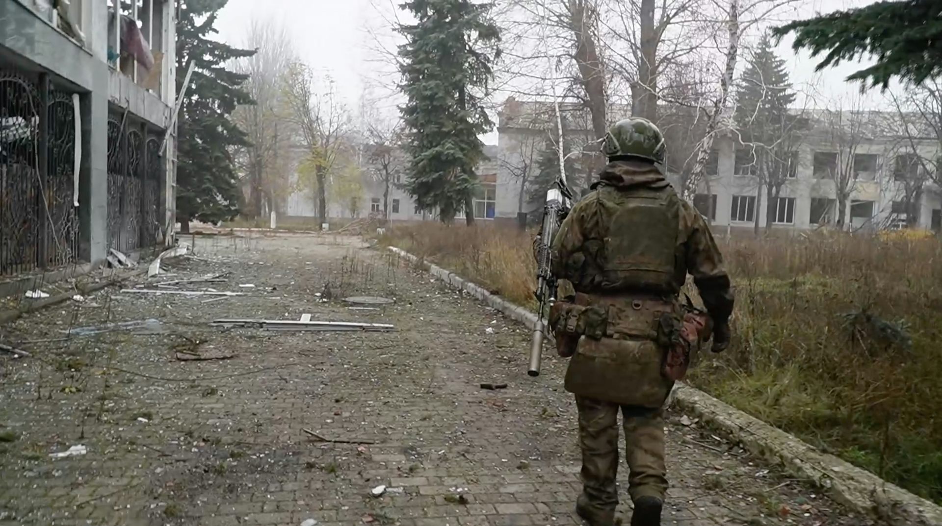 A soldier walks down a road surrounded by bombed-out buildings