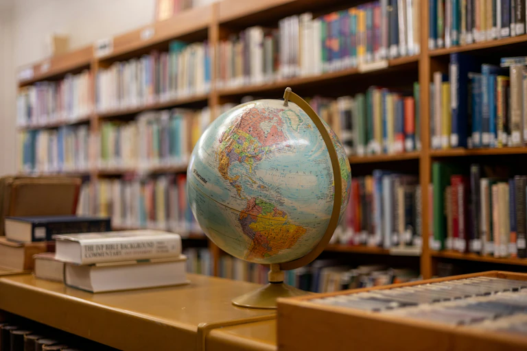 A globe on a shelf next to stacks and shelves of books.