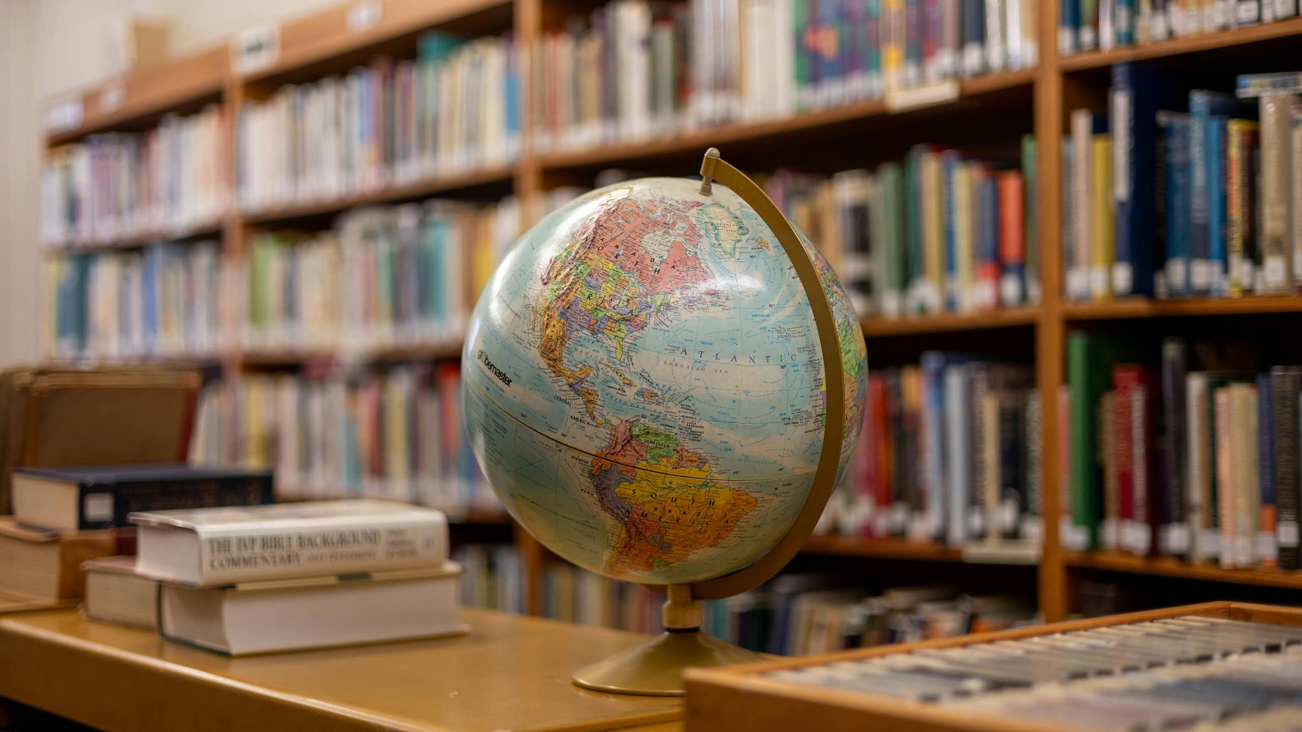 A globe on a shelf next to stacks and shelves of books.