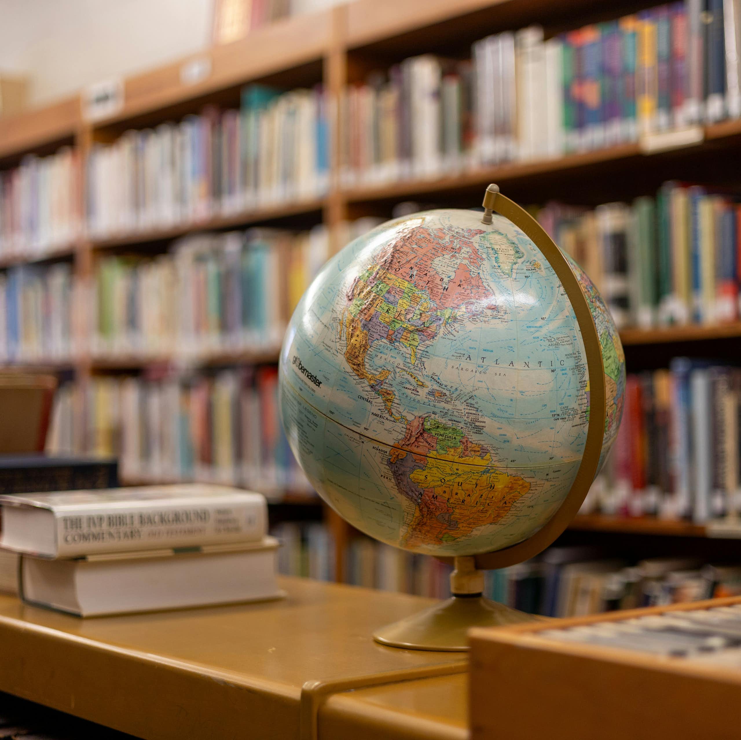 A globe on a shelf next to stacks and shelves of books.