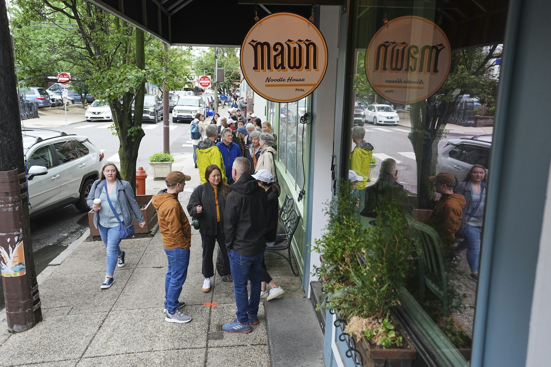 Line of people form on sidewalk outside a business with a circular sign that says 'Mawn'