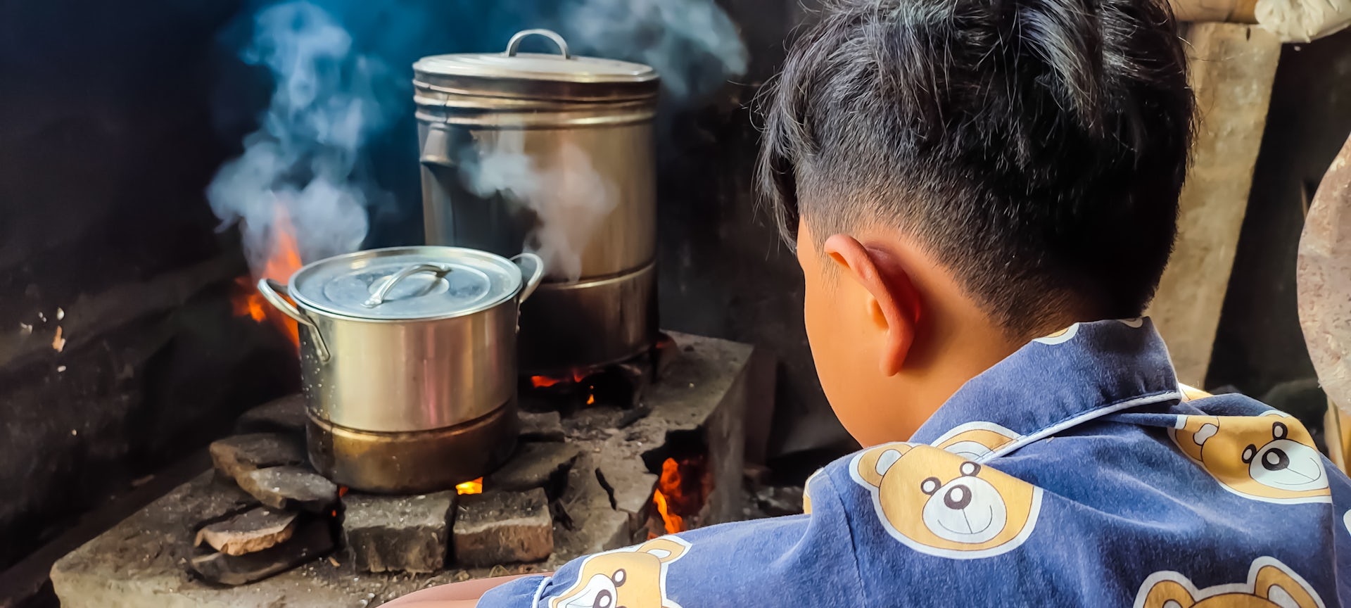 Young man watches over pots and pans cooking on a wood burning stove 