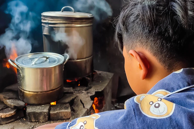 Young man watches over pots and pans cooking on a wood burning stove