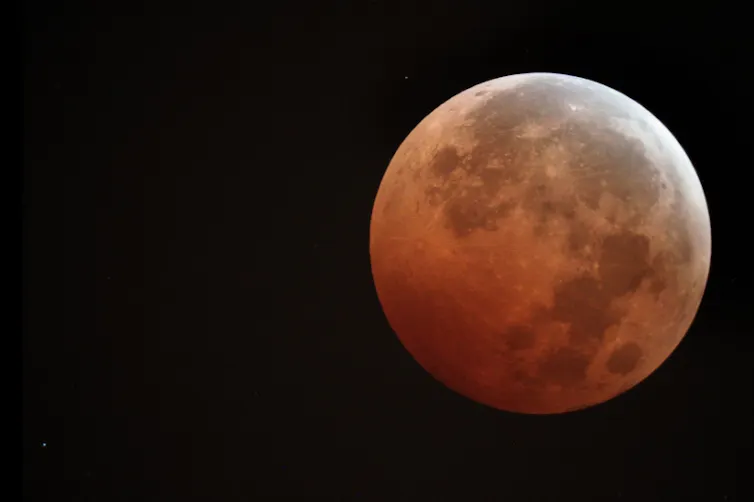 A full Moon, tinged orange from sunlight, during a lunar eclipse.