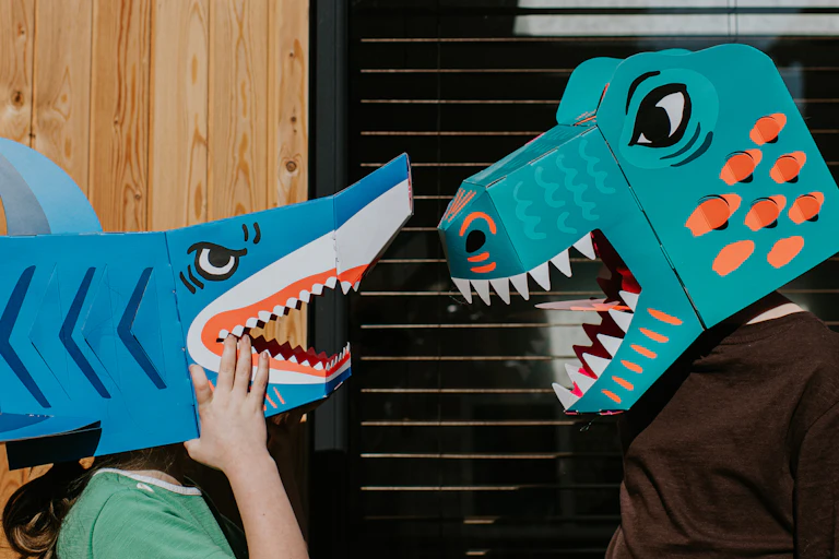 Two people in an angry shark and dinosaur cardboard mask face off each other.