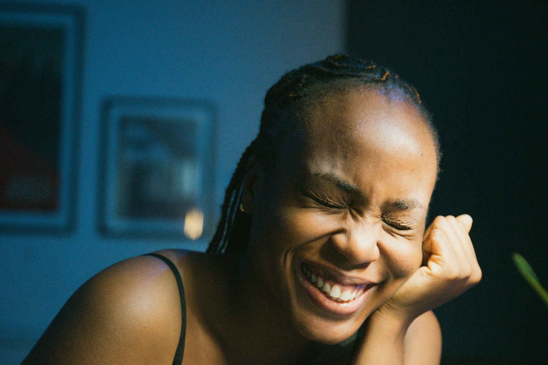 A black woman with braids looks embarrassed as she smiles with eyes closed.