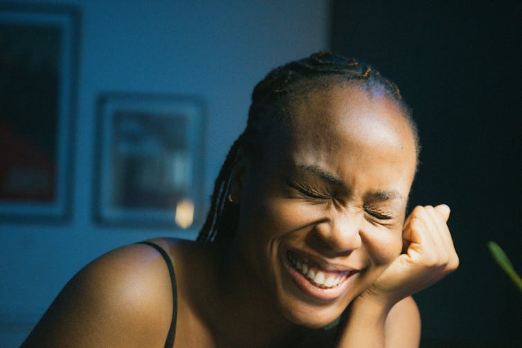A black woman with braids looks embarrassed as she smiles with eyes closed.