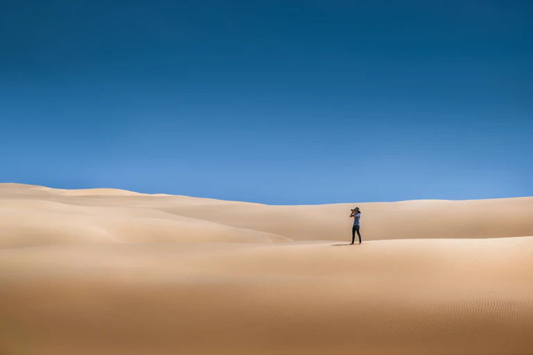 Person alone in desert, far away in distance, blue sky, reddish sand