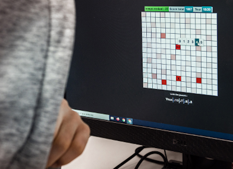 Un homme de dos regarde un écran où apparaît une grille avec des chiffres de 1 à 99