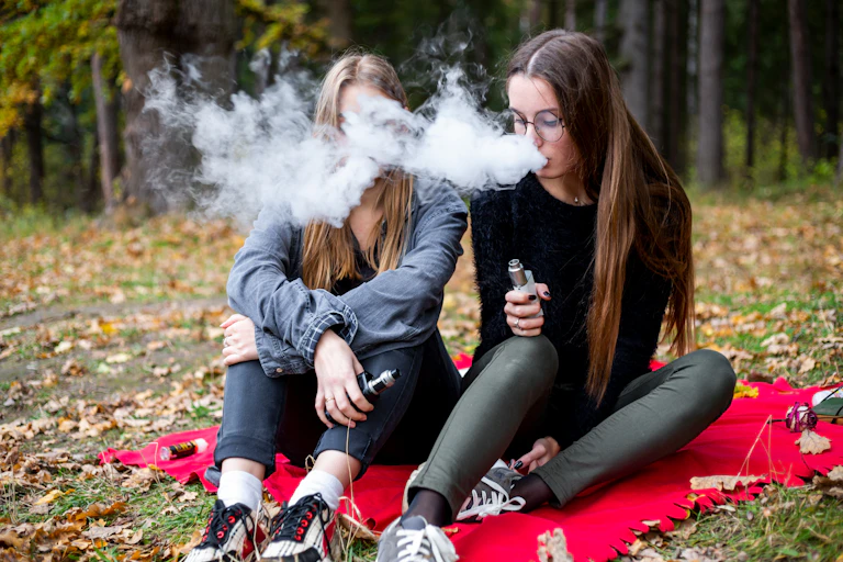 Two teenage girls vaping in park